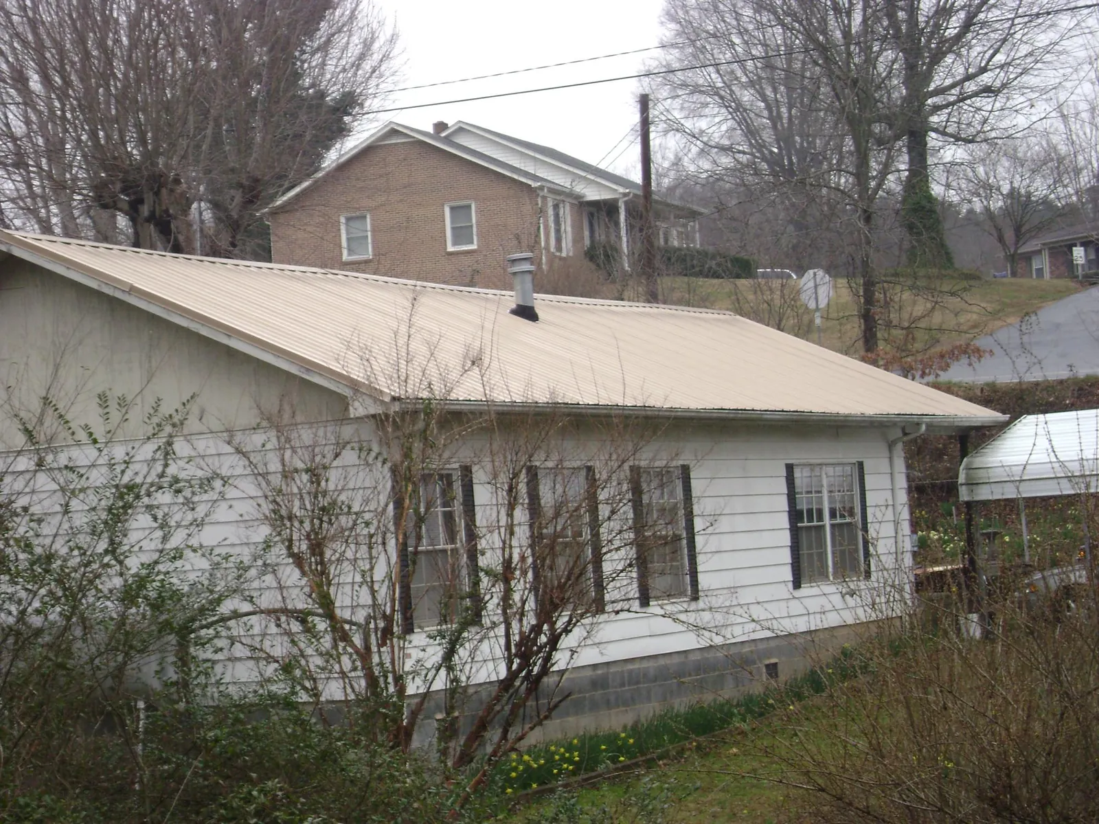 Tan metal roof on a white sided house set into a hillside — Commercial Roofing by Roofing Brothers in Lee